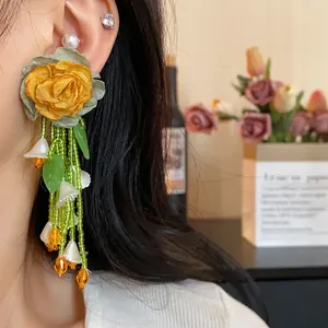Close-up of forest style yellow rose earrings with green bead tassels on an Asian model