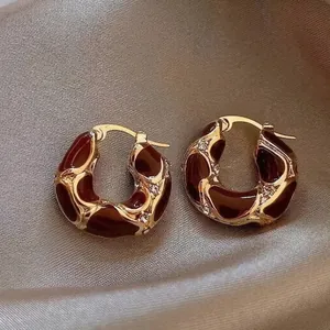 Detailed view of gold chunky hoop earrings featuring burgundy enamel and crystals.