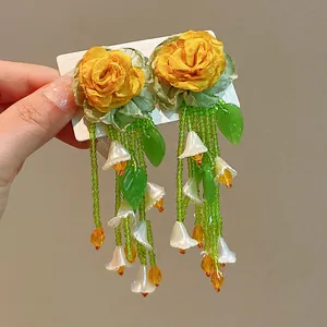 Macro close-up of handmade yellow rose floral earrings with green beaded long tassels