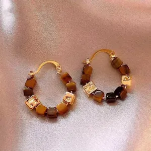 Close-up of bohemian gold hoop earrings featuring tiger's eye stone and metal cubes