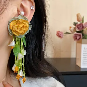 Close-up of forest-style flower earrings with green beaded tassels and yellow rose