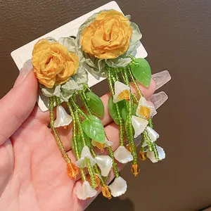 Close-up detail of forest-style flower tassel earrings with green beads and white charms