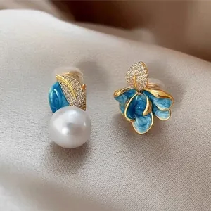 Macro detail of luxury asymmetric earrings featuring blue enamel and a large white pearl.