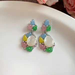 Primer plano de pendientes de resina de colores con cabujón blanco ovalado y cristales finos