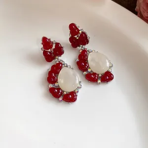 Detalle de pendientes vintage de resina roja con piedra blanca en forma de lágrima