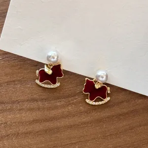 Primer plano de pendientes de caballito de madera rojos con perlas y pedrería fina.