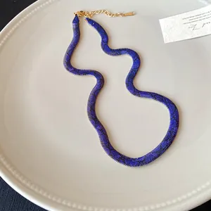 Primer plano del collar gargantilla azul con patrón de piel de serpiente y cierre dorado.