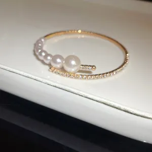 Close-up detail of an elegant gold open bangle featuring graduated pearls and fine rhinestones