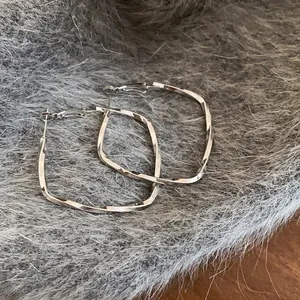 Elegant silver-colored twisted square hoop earrings presented on a soft grey fur background