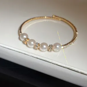 Macro close-up of gold open bangle with white pearls and crystal rhinestone spacers