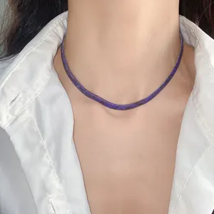 Primer plano de un collar choker plano morado con patrón de serpiente y camisa blanca.