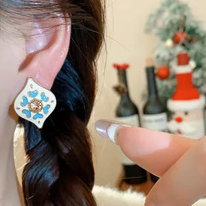 Close-up of vintage white enamel earring with blue heart pattern and central rhinestone