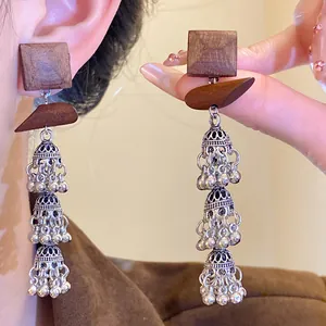 Close-up of hand holding vintage ethnic wooden square tassel earrings in bohemian style