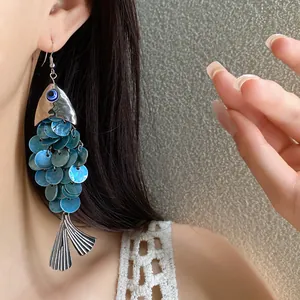 Gros plan d'une boucle d'oreille vintage en forme de poisson avec écailles bleues portées