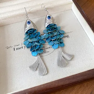 Vue détaillée de boucles d'oreilles en forme de poisson avec écailles bleues et nazar.