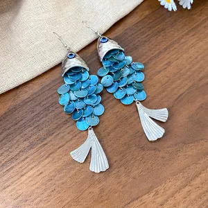 Gros plan de boucles d'oreilles poisson uniques avec écailles bleues et queue argentée