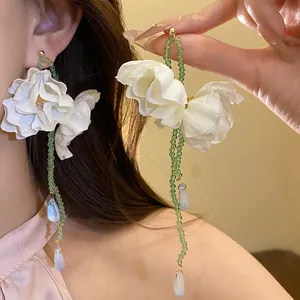Exquisite detail of white fabric flower earrings with green bead tassels worn by a model