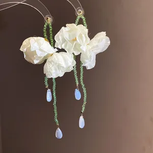 Detail of elegant white fabric flower earrings with green beaded tassels.