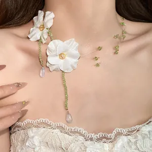 Close-up of elegant white fabric flower necklace with green beads on model's neck.