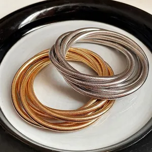 Multi-layer metal spring bracelets in gold and silver finishes on a ceramic plate