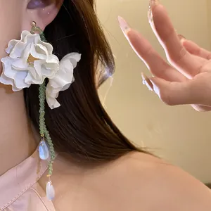 Close-up of elegant white fabric flower tassel earrings worn by a model for a sweet vacation look.