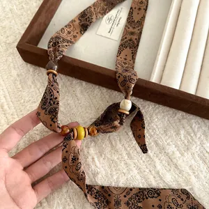 Macro view of bohemian paisley print fabric scarf necklace featuring artistic decorative beads