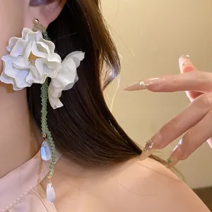 Close-up of elegant white fabric flower earrings with green beaded tassels on model