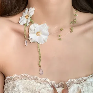 Detailed view of an elegant white fabric flower necklace with green beads and clear drop pendants.