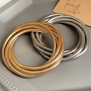 Detailed close-up showing gold and silver multilayer spring bangles on a gray textured tray