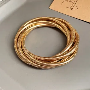 Detail shot of multi-layer golden spring bangle bracelets on a grey minimalist tray