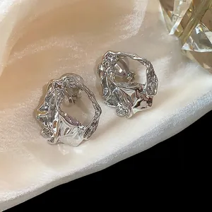 Detail showing silver pleated geometric clip-on earrings on elegant satin fabric.