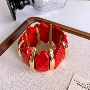 Dettaglio ravvicinato di bracciale a maglie grosse in acrilico rosso e metallo dorato.
