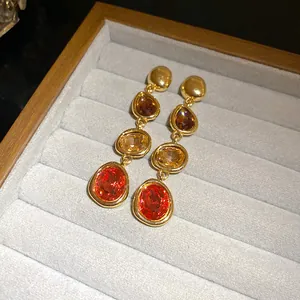 Detailed view of French court style gold earrings with red and amber gradient gemstones