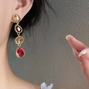 Close-up of elegant gold drop earrings with multi-colored gemstones worn by a model in detail.