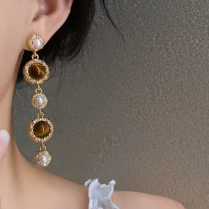 Detail view of French royal style drop earrings with pearls and amber resin on model.
