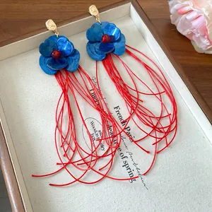 Nahaufnahme blauer Acrylblumen-Ohrringe mit langen roten Schnurquasten im Vintage-Stil.
