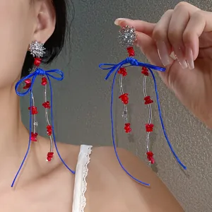 Nahaufnahme von Retro-Silberquasten-Ohrringen mit blauen Kordelschleifen und roten Perlen