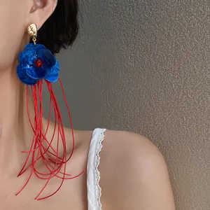 Detailaufnahme von Vintage-Ohrringen mit blauer Acrylblüte und langen roten Quasten