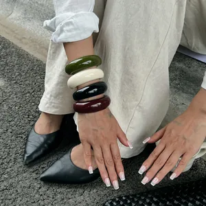 Macro view of four colorful chunky resin bangles worn on a wrist in a stylish outdoor setting.