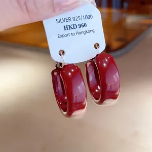 Macro detail view of burgundy red enamel hoop earrings with silver needle on display card.