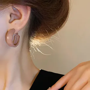 Detailed close-up view of a retro C-shaped brown enamel hoop earring worn on an ear