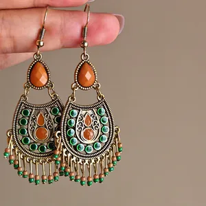 Close-up of bohemian vintage drop earrings with green and orange bead tassels