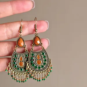 Close-up of vintage bohemian tassel earrings with orange and green beads held by hand