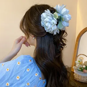 Detail view of a sweet blue fabric flower hair claw clip worn on long wavy brown hair.