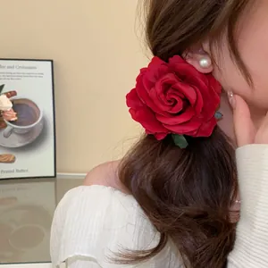 Detailed close-up view of an elegant red fabric rose hair claw clip worn on wavy hair.