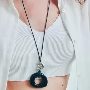 Close-up detail of minimalist black resin circular pendant necklace worn on a fashion model