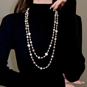 Detail showing a long pearl necklace with crystal flower charms on a black sweater.