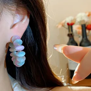 Primer plano de pendientes de aro con cuentas de resina púrpura y azul en la oreja