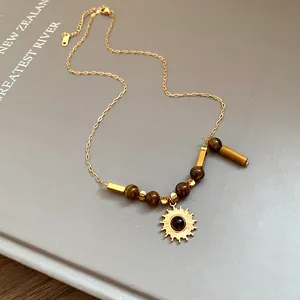 Close-up of the sun pendant and tiger eye beads on a gold chain necklace.