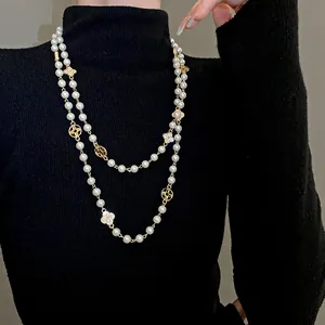 Detailed view of a long pearl necklace featuring rhinestone flower charms on a black sweater